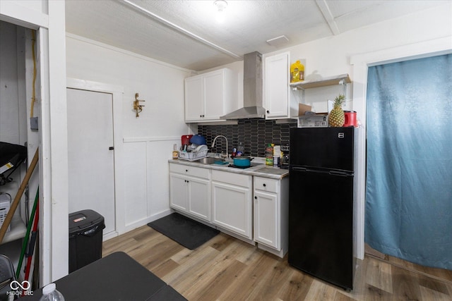 kitchen featuring white cabinets, wall chimney exhaust hood, light wood-style flooring, freestanding refrigerator, and light countertops