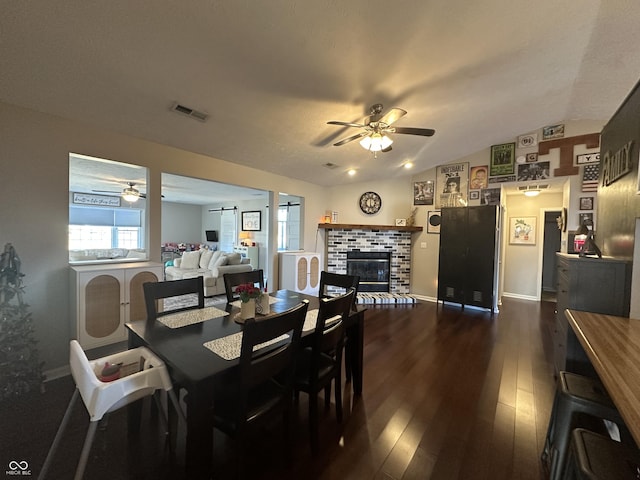 dining space featuring visible vents, a ceiling fan, dark wood-style floors, vaulted ceiling, and a brick fireplace