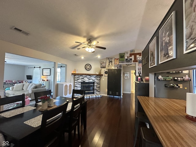 dining room with a barn door, visible vents, a ceiling fan, dark wood-type flooring, and a fireplace