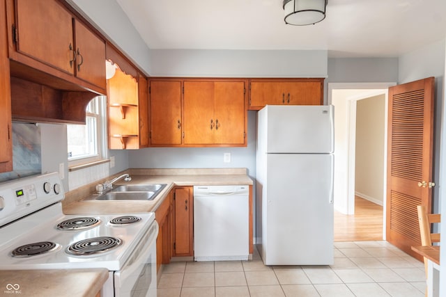 kitchen with light tile patterned floors, white appliances, a sink, light countertops, and brown cabinets