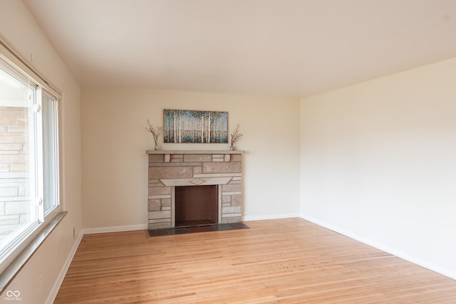 unfurnished living room with a stone fireplace, baseboards, and wood finished floors