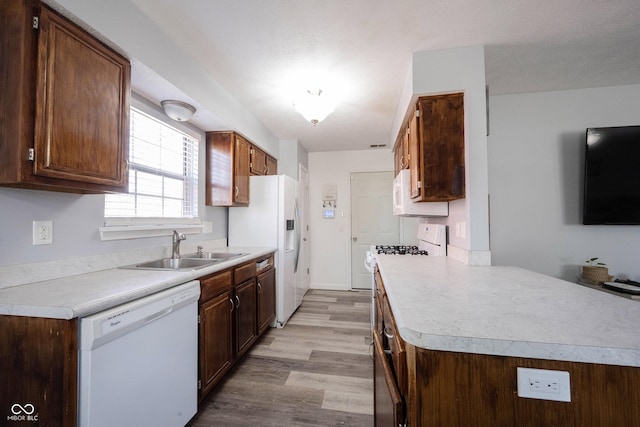 kitchen featuring light wood finished floors, light countertops, a peninsula, white appliances, and a sink