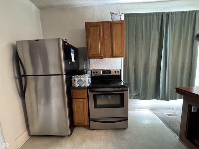 kitchen with appliances with stainless steel finishes, dark countertops, brown cabinetry, and light floors