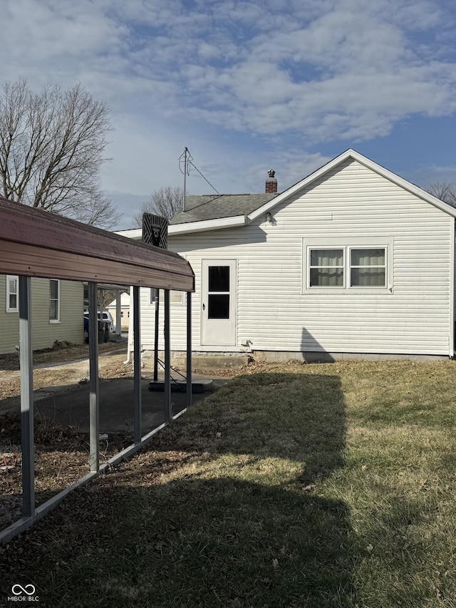 rear view of property featuring a chimney, a lawn, and a detached carport