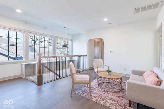 living area with arched walkways, recessed lighting, visible vents, an upstairs landing, and wood finished floors