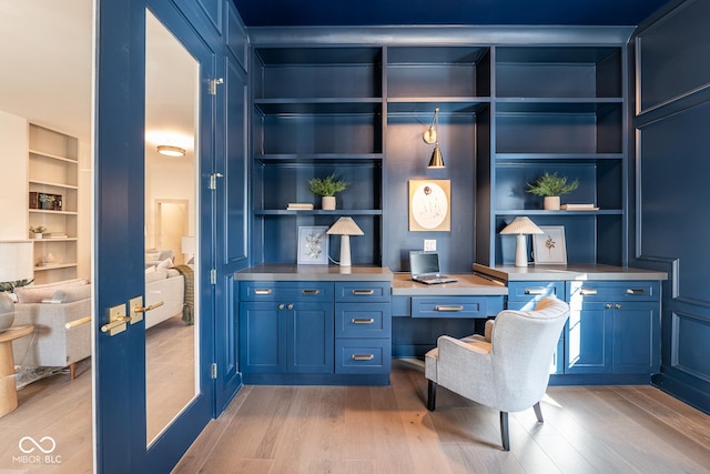 home office featuring built in features, light wood-style flooring, built in desk, and a decorative wall