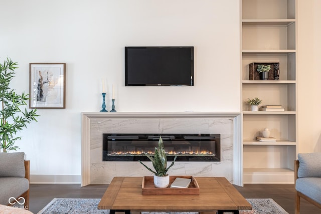 living room with baseboards, a premium fireplace, built in features, and wood finished floors