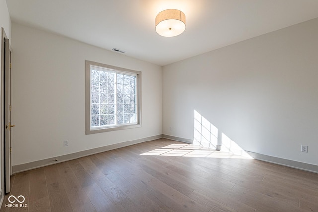 unfurnished room featuring wood finished floors, visible vents, and baseboards