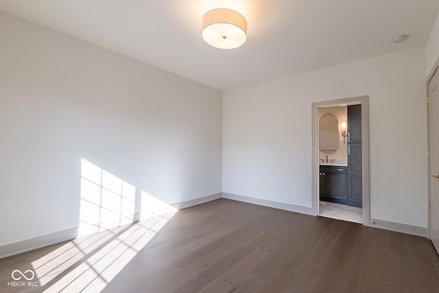 unfurnished room with dark wood-style flooring, a sink, and baseboards