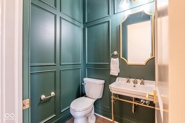 half bathroom featuring toilet, a decorative wall, and a sink