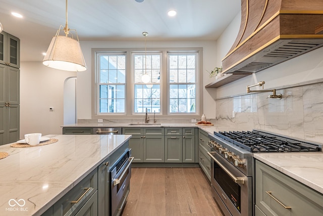 kitchen featuring light wood-style flooring, appliances with stainless steel finishes, a sink, light stone countertops, and wall chimney exhaust hood