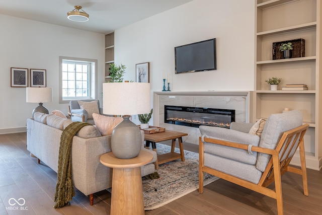 living room featuring built in shelves, a fireplace, baseboards, and wood finished floors