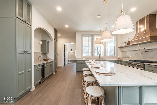 kitchen featuring beverage cooler, custom range hood, high end range, light wood-type flooring, and a sink