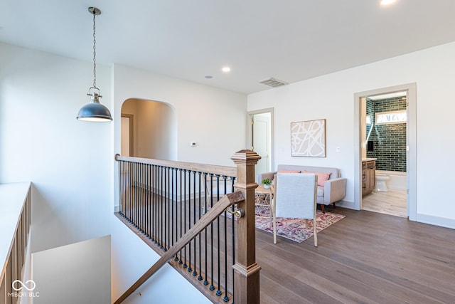 corridor featuring arched walkways, recessed lighting, visible vents, an upstairs landing, and wood finished floors