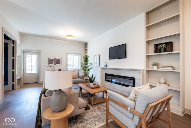 living area featuring built in shelves, a high end fireplace, wood-type flooring, and baseboards