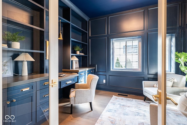 home office with wood finished floors, built in study area, visible vents, and a decorative wall