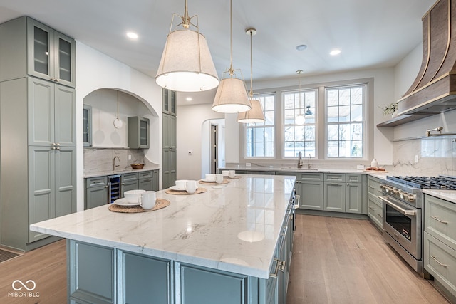 kitchen featuring light wood finished floors, custom range hood, gray cabinetry, beverage cooler, and high end stove