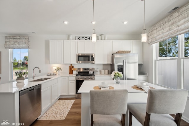 kitchen featuring pendant lighting, stainless steel appliances, light countertops, dark wood-type flooring, and a sink