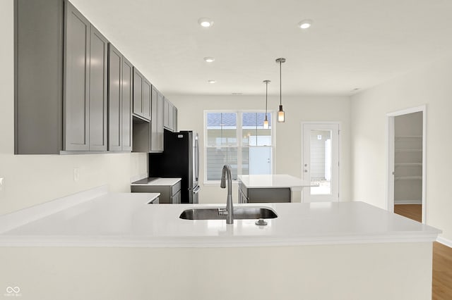 kitchen featuring gray cabinets, light countertops, freestanding refrigerator, a kitchen island, and a sink