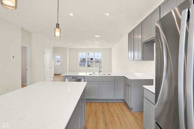 kitchen with appliances with stainless steel finishes, gray cabinets, a sink, and light wood finished floors