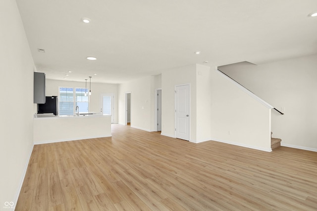 unfurnished living room featuring light wood-style floors, recessed lighting, a sink, and stairway