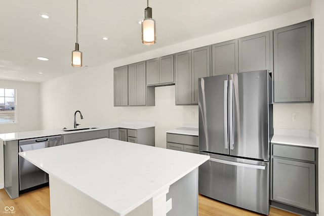 kitchen with a peninsula, a sink, appliances with stainless steel finishes, light wood-type flooring, and gray cabinets