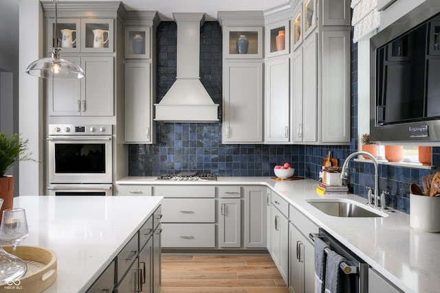 kitchen featuring gray cabinetry, stainless steel appliances, a sink, light wood-style floors, and wall chimney exhaust hood