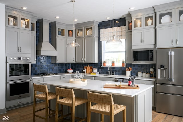 kitchen with wood finished floors, stainless steel appliances, light countertops, wall chimney range hood, and a sink