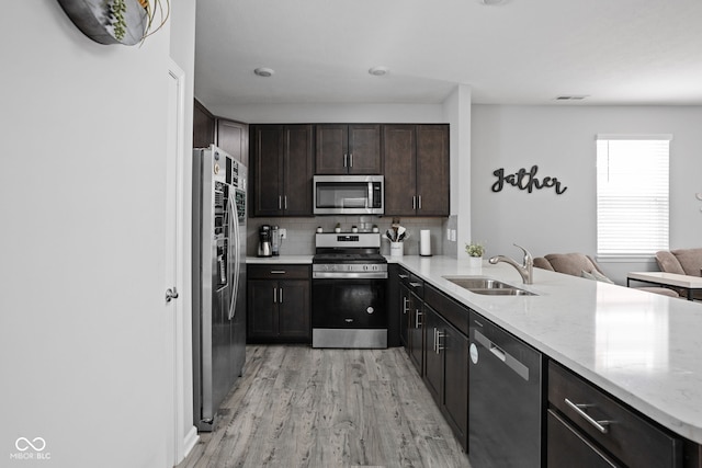 kitchen with tasteful backsplash, appliances with stainless steel finishes, light wood-style floors, a sink, and dark brown cabinetry