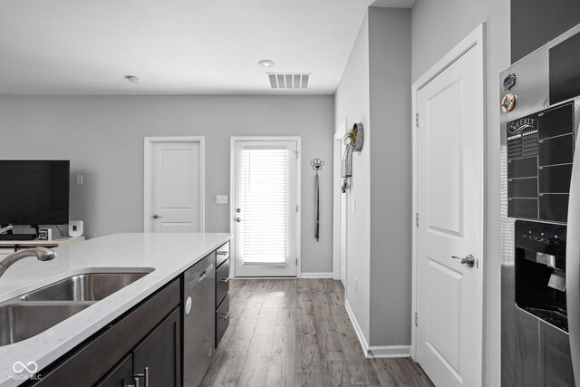 kitchen featuring visible vents, dishwasher, light stone counters, wood finished floors, and a sink