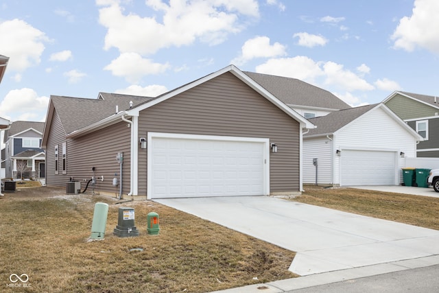 view of front of house with a garage, driveway, central AC unit, roof with shingles, and a front lawn