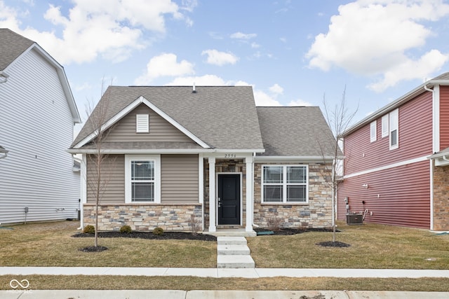 view of front of house with stone siding, roof with shingles, central AC, and a front yard