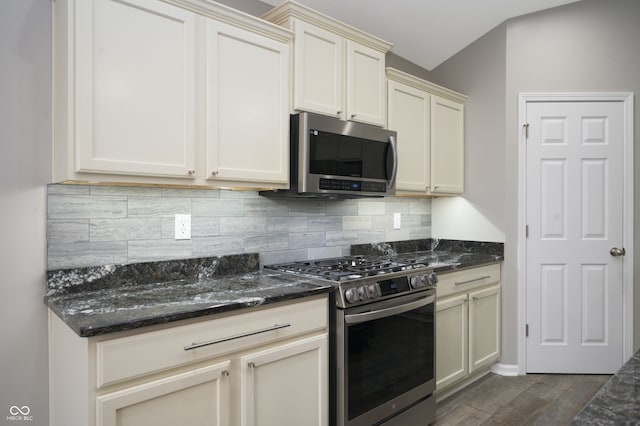 kitchen with tasteful backsplash, appliances with stainless steel finishes, dark wood finished floors, and dark stone counters