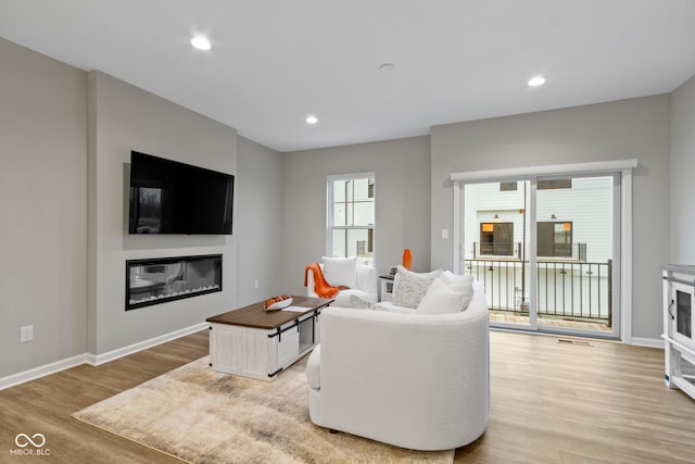 living area with light wood finished floors, recessed lighting, and a glass covered fireplace