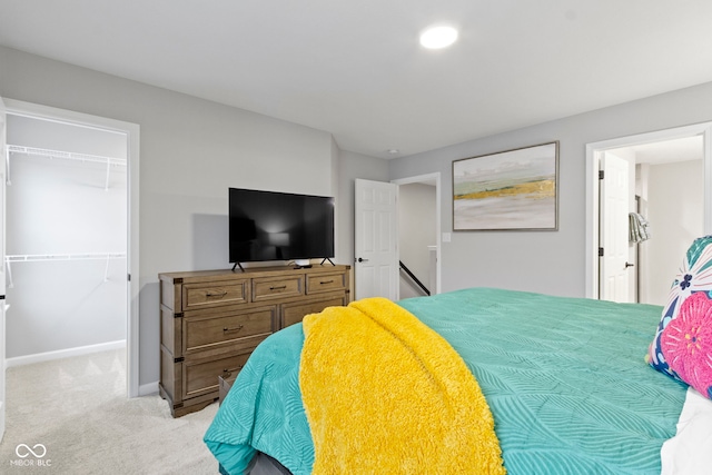 bedroom with baseboards, a walk in closet, a closet, and light colored carpet