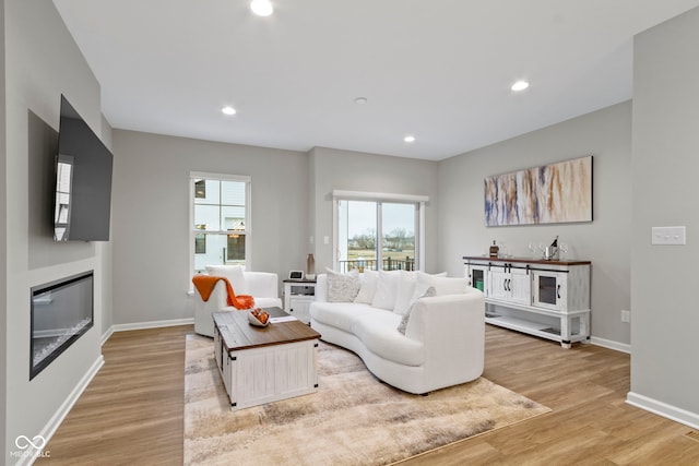 living room featuring a glass covered fireplace, light wood-style flooring, and recessed lighting