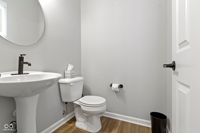 half bathroom with wood finished floors, toilet, and baseboards