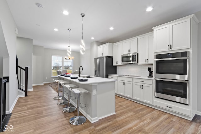 kitchen featuring a kitchen island with sink, stainless steel appliances, white cabinets, light wood-style floors, and tasteful backsplash