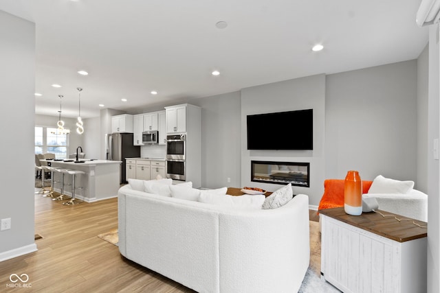 living room with a glass covered fireplace, baseboards, light wood finished floors, and recessed lighting