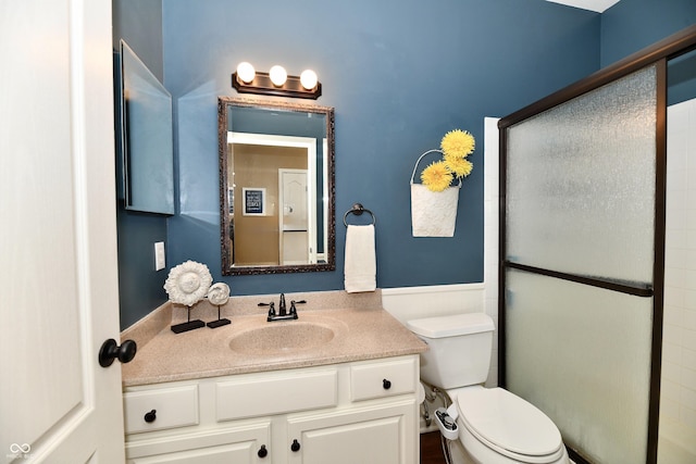 bathroom featuring vanity, toilet, a shower with shower door, and wainscoting