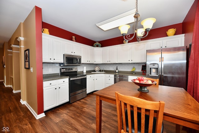 kitchen featuring dark countertops, appliances with stainless steel finishes, an inviting chandelier, dark wood-style floors, and white cabinetry