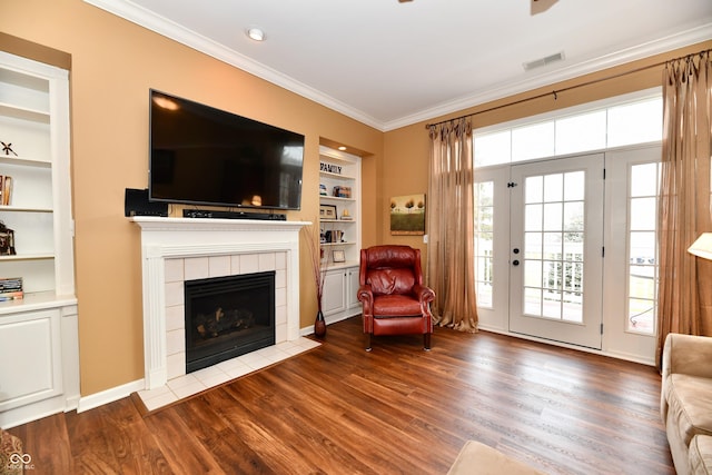 living area featuring visible vents, a tiled fireplace, built in features, dark wood finished floors, and crown molding