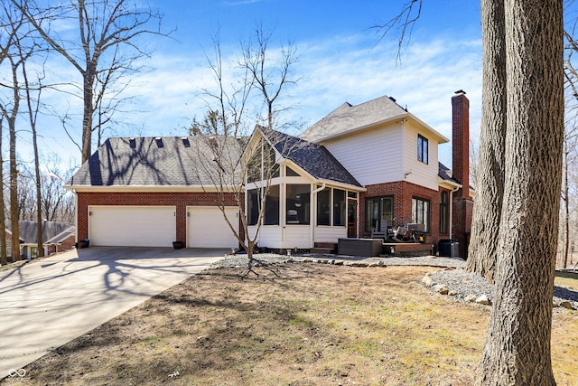 view of front of property with brick siding, concrete driveway, a chimney, a sunroom, and an attached garage