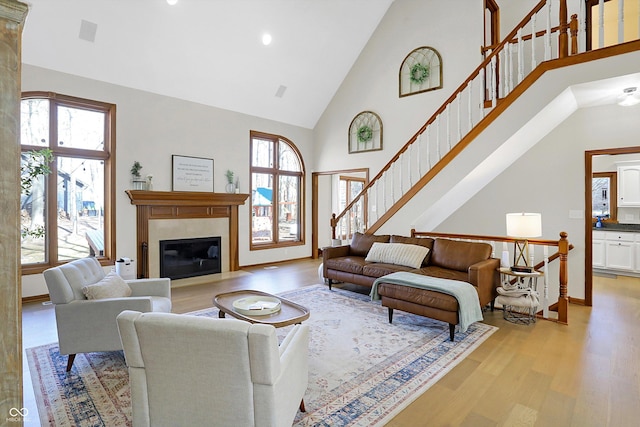 living area featuring plenty of natural light, high vaulted ceiling, light wood-style flooring, and a fireplace with flush hearth