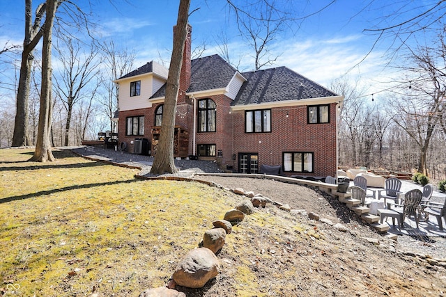 rear view of property with brick siding, central AC, a shingled roof, and a yard