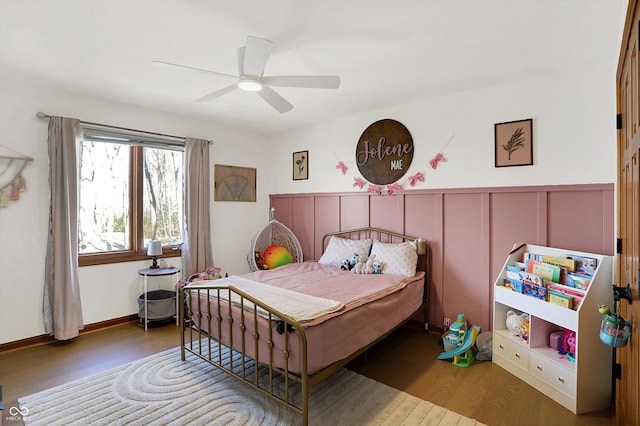 bedroom featuring a decorative wall, wood finished floors, wainscoting, and ceiling fan