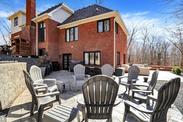 back of house featuring roof with shingles, outdoor lounge area, brick siding, a chimney, and a patio area