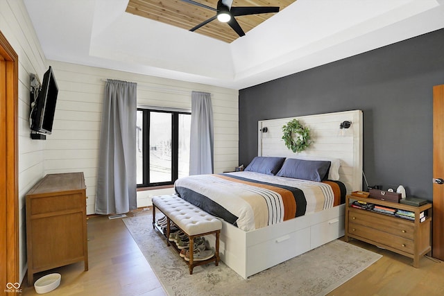 bedroom featuring wooden walls, wood ceiling, light wood-style flooring, a raised ceiling, and a ceiling fan