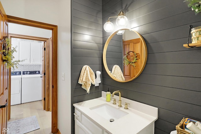 half bath featuring independent washer and dryer, vanity, and wood walls