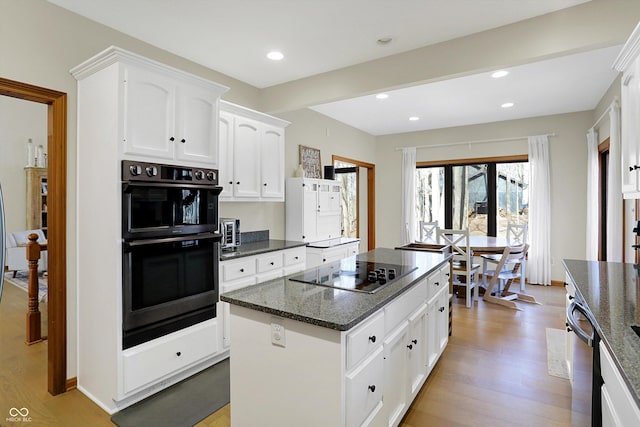 kitchen featuring light wood-type flooring, black appliances, dark stone countertops, a center island, and white cabinets